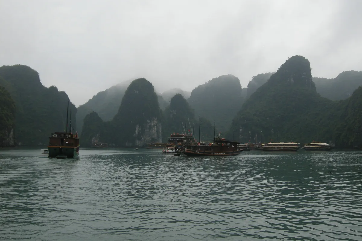 Wooden junk boats drift among misty limestone karsts in Ha Long Bay. Wooden junk boats drift among misty limestone karsts in Ha Long Bay.