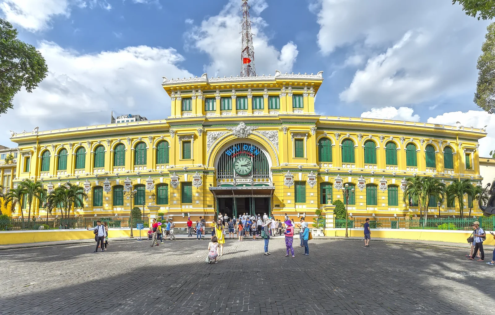 Yellow French colonial facade of Saigon Central Post Office with visitors gathered on the plaza below. Yellow French colonial facade of Saigon Central Post Office with visitors gathered on the plaza below.